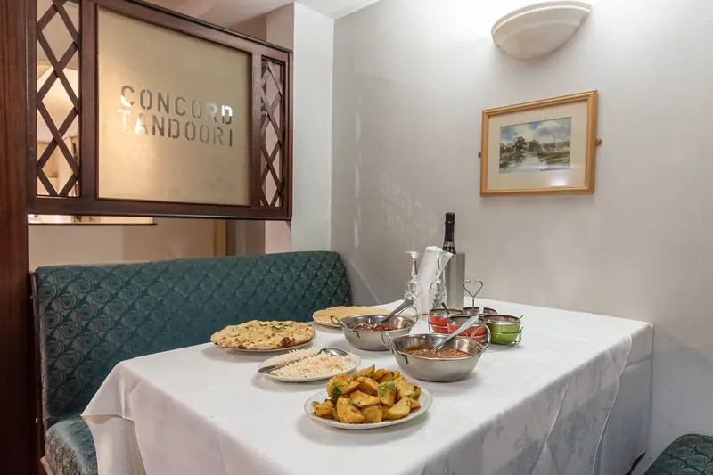 A dining booth at Concord Tandoori with the restaurant’s name on the wall and dishes on the table