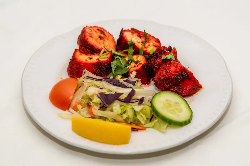 Chicken tikka with salad and a lemon wedge on a white plate