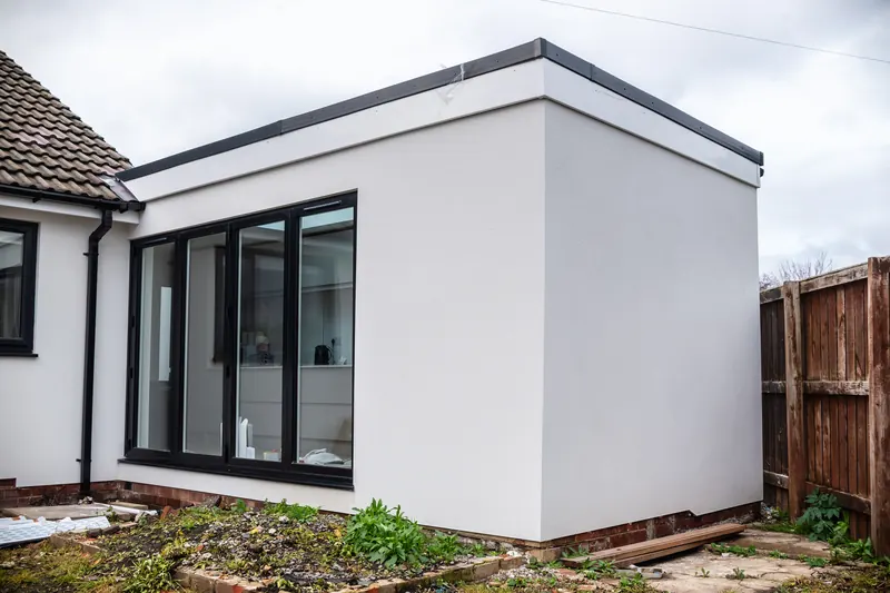 White rendered single-storey extension with black-framed glazing, nearly finished