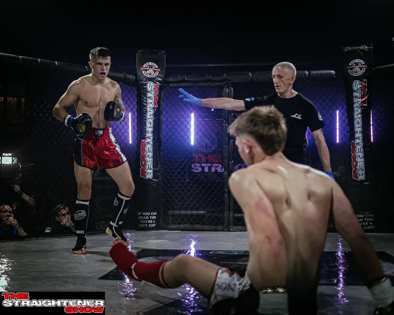 Kickboxer landing a kick as his opponent goes down in the cage