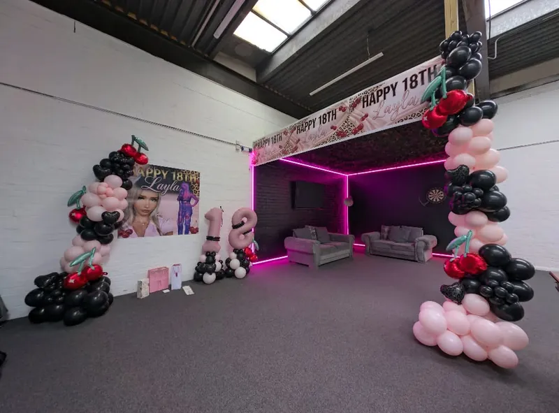 The studio lounge set lit pink for a birthday party, with pink, black and red cherry balloon arches