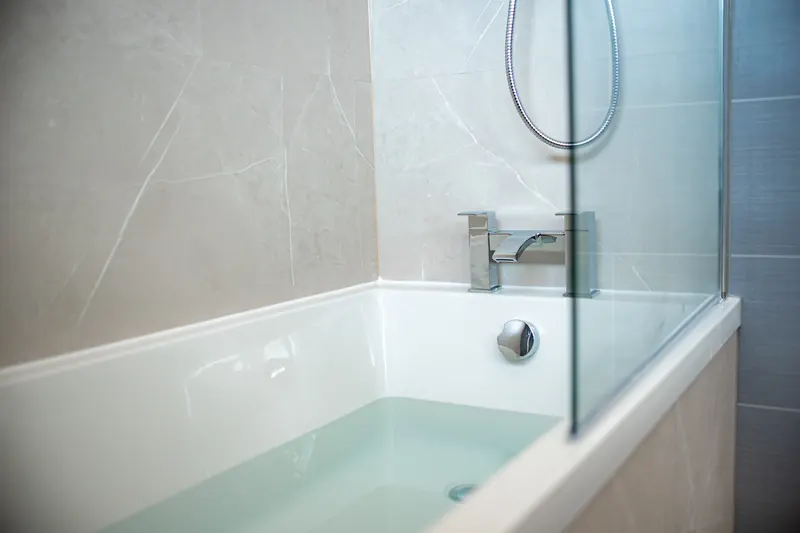 White bath with a glass shower screen and chrome taps
