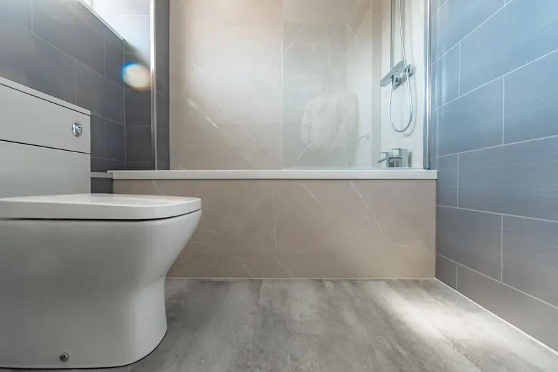 A finished bathroom with a wall-hung toilet, vanity unit and bath with shower