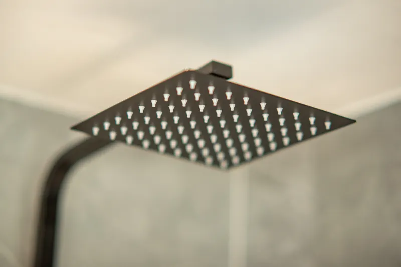 Black square rainfall shower head against grey tiles