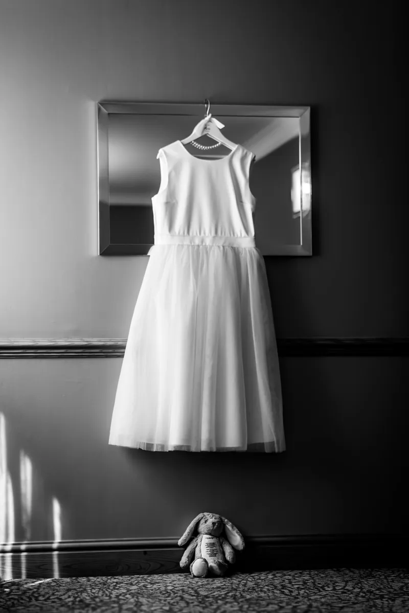 Black and white photo of a white dress hanging on a wall on a wedding morning