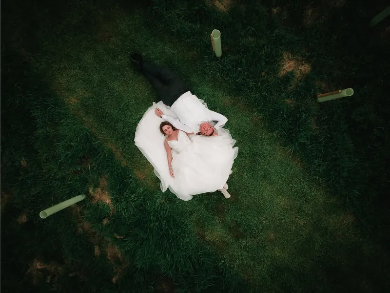 Drone photograph looking straight down on a bride and groom lying on the grass in her wedding dress