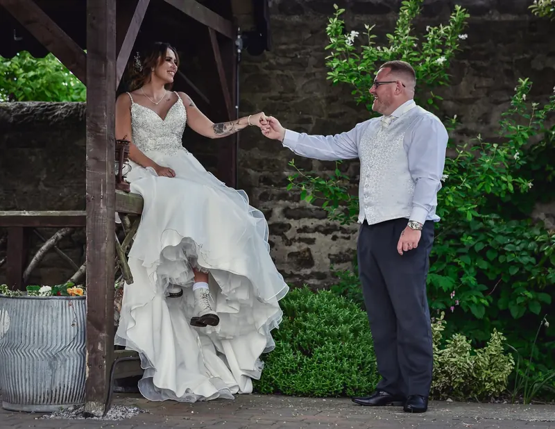 Bride sitting on a garden bench holding hands with her groom on their wedding day