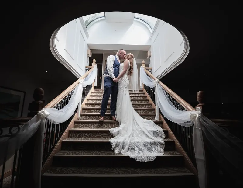 Bride and groom kissing at the top of a grand staircase with her long lace train flowing down the steps